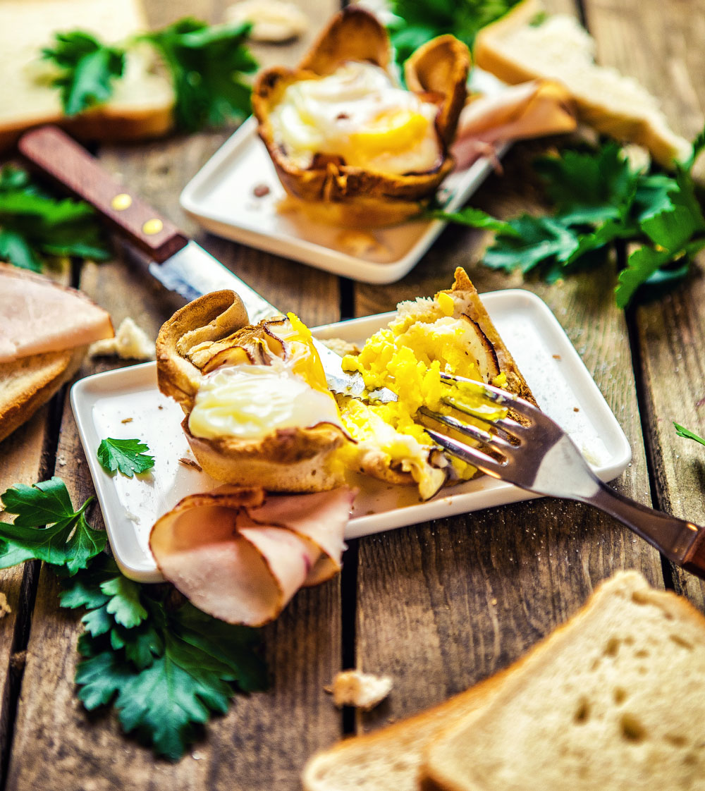 Zwei goldbraune Toastbrot-Ei-Muffins mit sichtbarem weichem Eigelb auf einem Teller